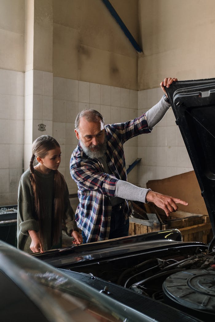Father teaching daughter about car mechanics in a garage setting.